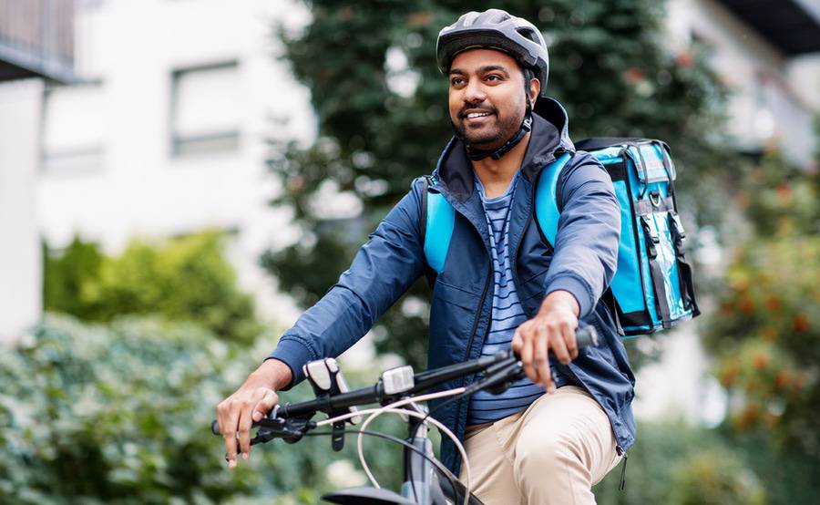 A young, black man bikes carrying a backpack and wearing appropriate helmet for safety.
