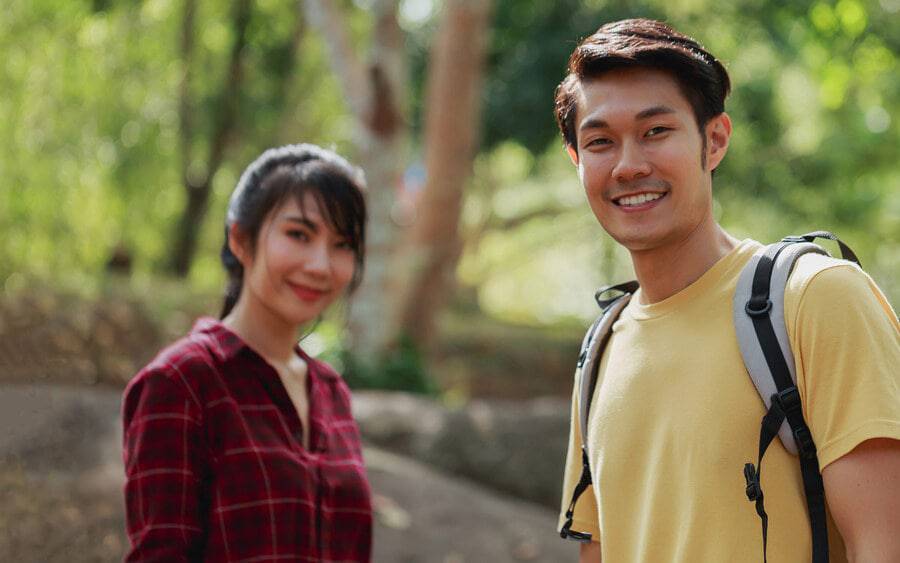 A man and a woman smiling while outside on a sunny day during a hike.
