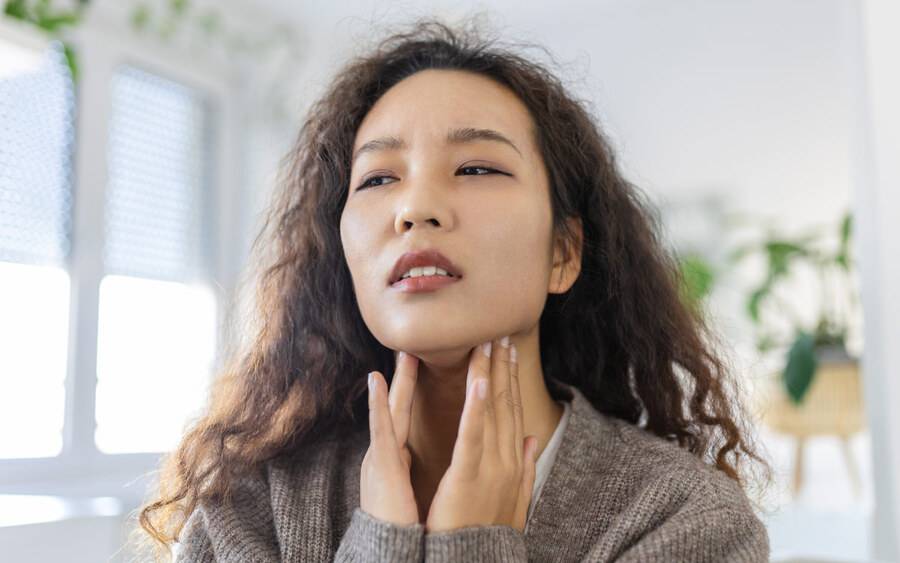 A young Asian woman touches her neck checking her thyroid gland.