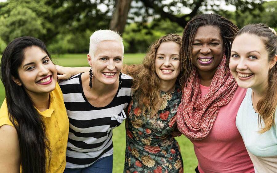 Five women stand arm in arm in a park, representing a range of ages and races with different cancer risks.