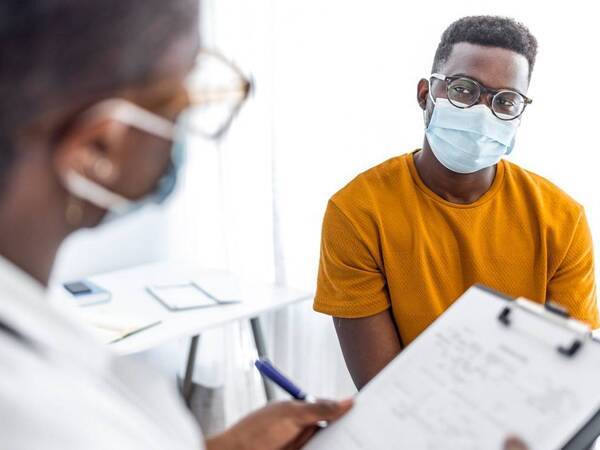 A young man listening to his doctor, both wearing medical masks