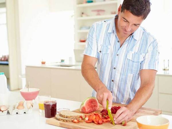A healthy man slices berries for a low-cholesterol meal in his kitchen. 