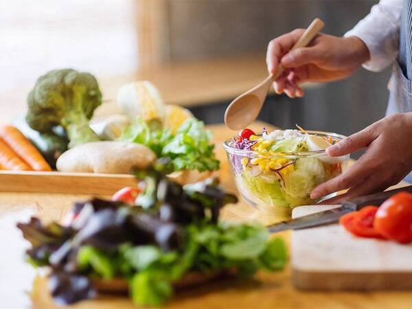 A healthy salad is being prepared with lettuce, tomatoes, carrots, corn and purple cabbage.